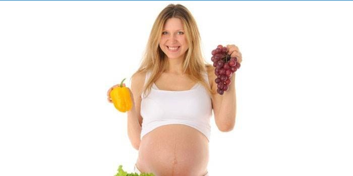 Een zwangere vrouw houdt peper en een tros druiven in haar handen