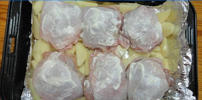 Kippendijen op een kussen van aardappelen voor het bakken op een bakplaat