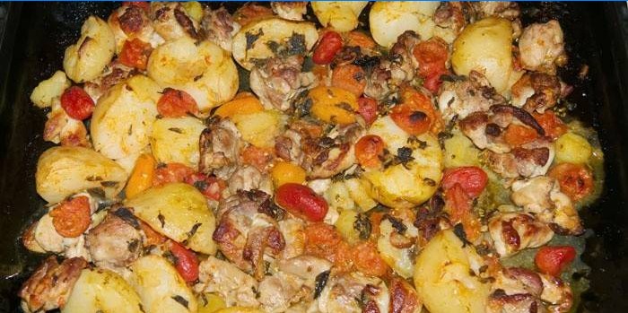 Kippenpoten met aardappelen en tomaten op een bakplaat