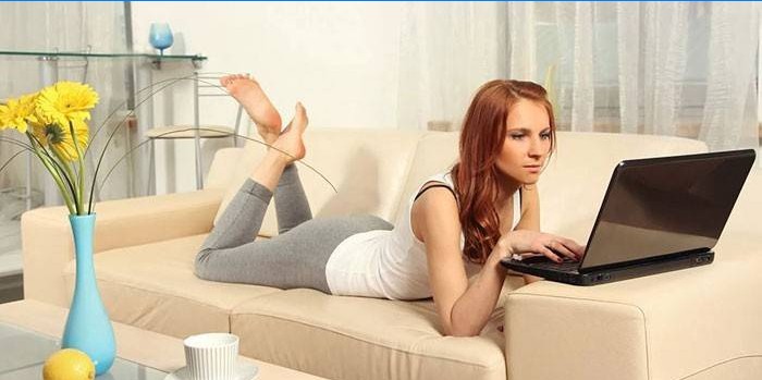 Het meisje ligt op een sofa met een laptop
